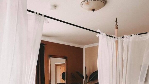 A bedroom with a canopy bed, a chair, a potted plant, and a wooden floor. - Hotel Ammerländer Hof (Westerstede)
