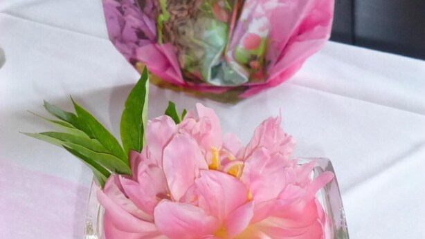 Un vase avec des fleurs roses et des feuilles vertes, posé sur une nappe blanche.