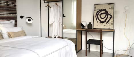 A modern bedroom with a large bed, a mirror, a side table with a lamp, and a framed abstract artwork.