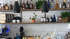 A bar area with shelves of liquor bottles, a coffee machine, and a variety of food and drink containers. - Casa Figa 39 (Zagreb)