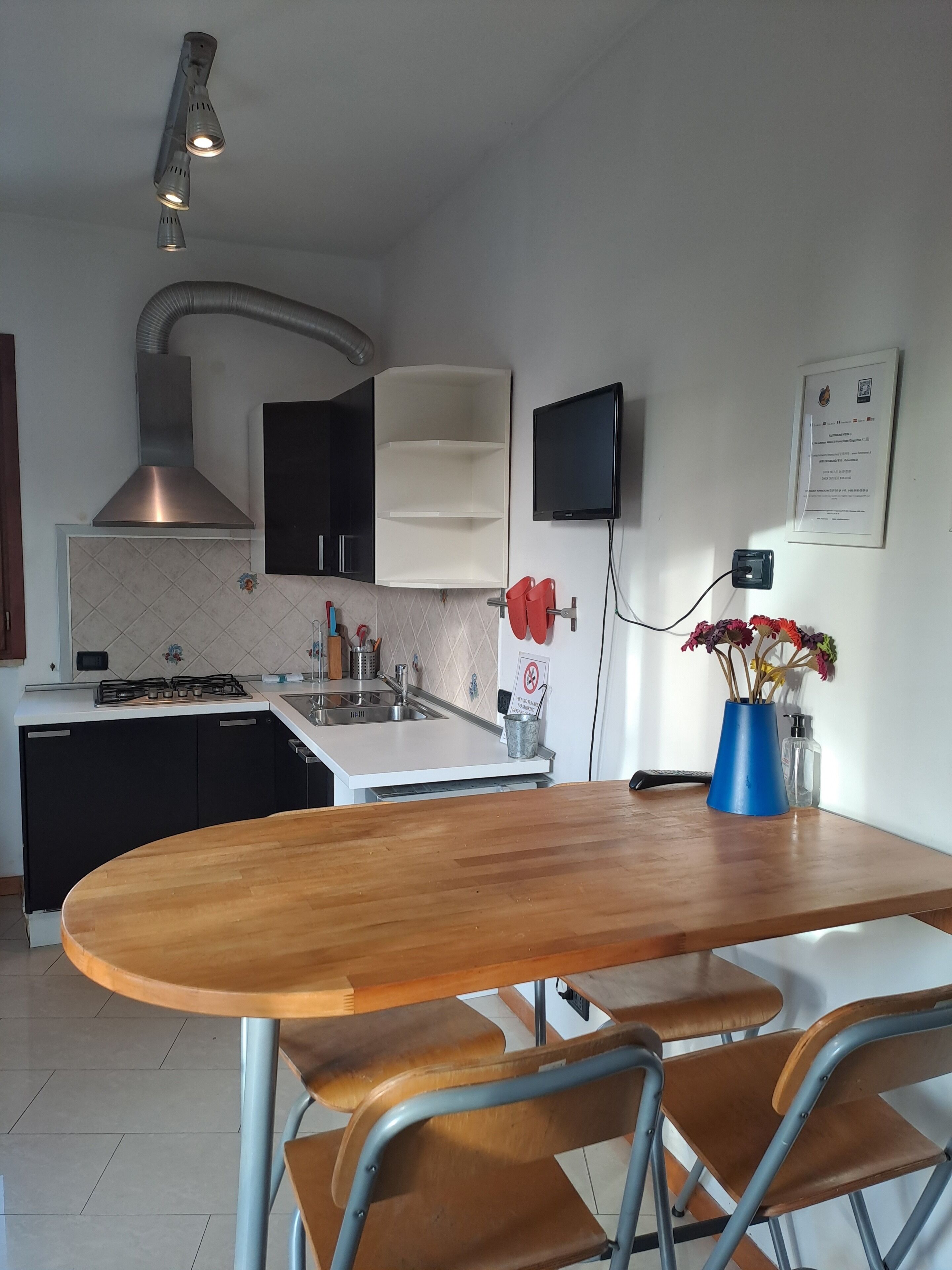 Uma cozinha moderna com uma mesa de madeira, cadeiras de metal, fogão a gás e coifa de aço inoxidável.