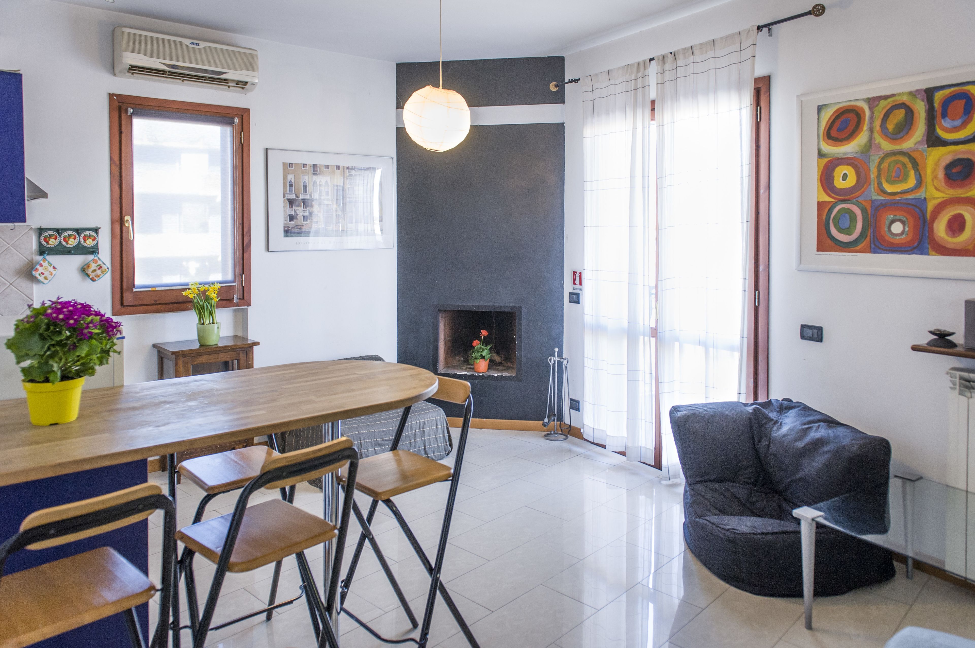 Una sala de estar moderna con chimenea, un comedor con una mesa y sillas de madera, y un sofá de cuero negro.