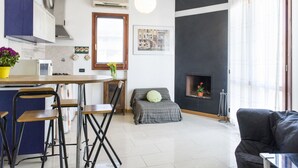 Ett kompakt bostadsutrymme med ett köksområde, ett matbord med stolar, en soffa och en öppen spis.