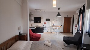 Ett hotellrum med en säng, ett skrivbord, en stol och ett litet kök i bakgrunden.