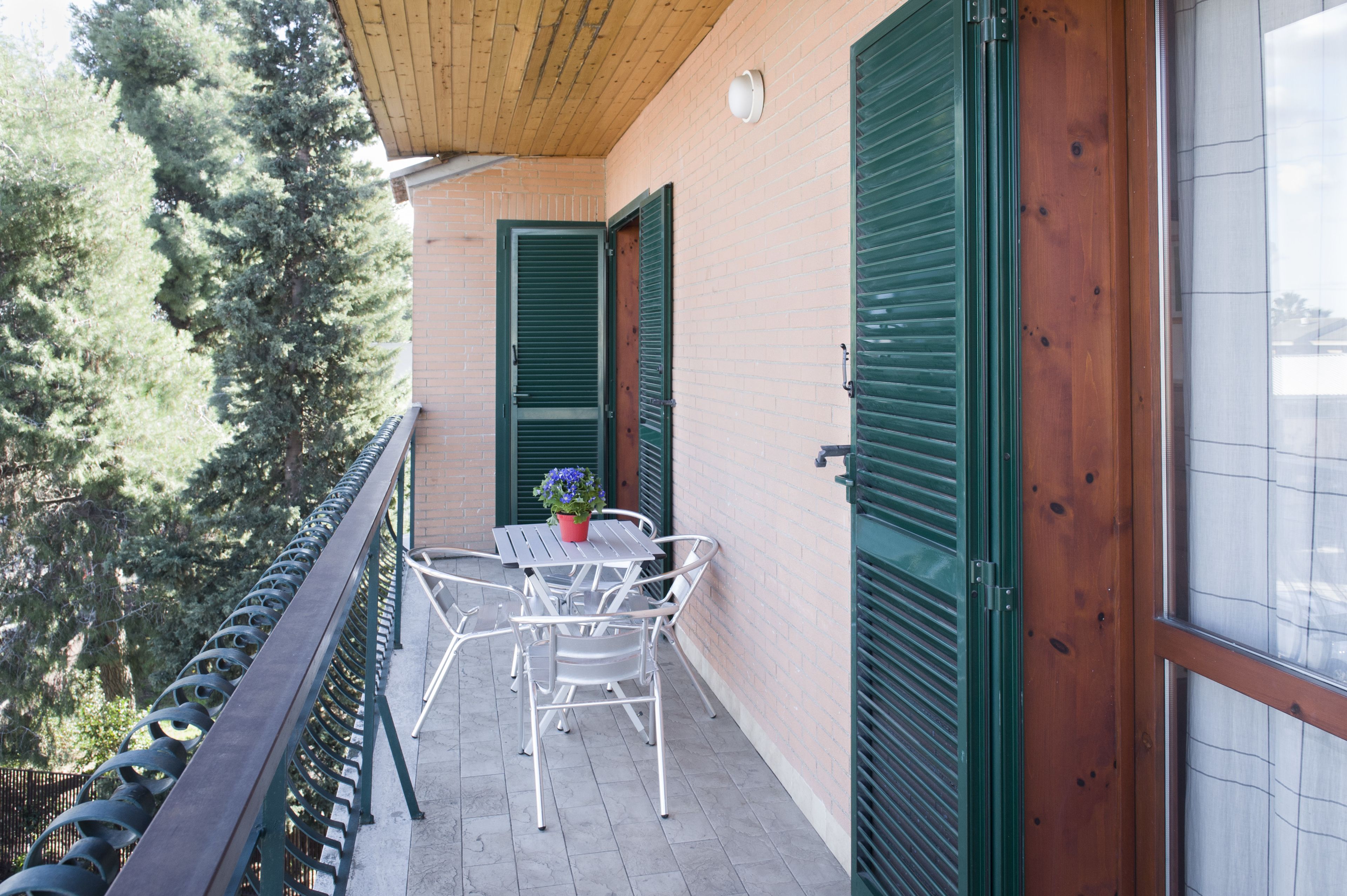 Un balcon avec une table et des chaises, des volets verts et une vue sur les arbres.