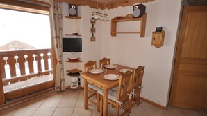 Un coin repas avec une table en bois dressée pour quatre personnes, un téléviseur fixé au mur et un balcon doté d’une balustrade en bois.