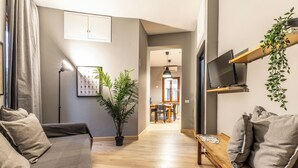 A modern living room with a sofa, a coffee table, and a TV on a shelf. There is a plant and a framed picture on the wall. - Flatinrome Trastevere (Rome)