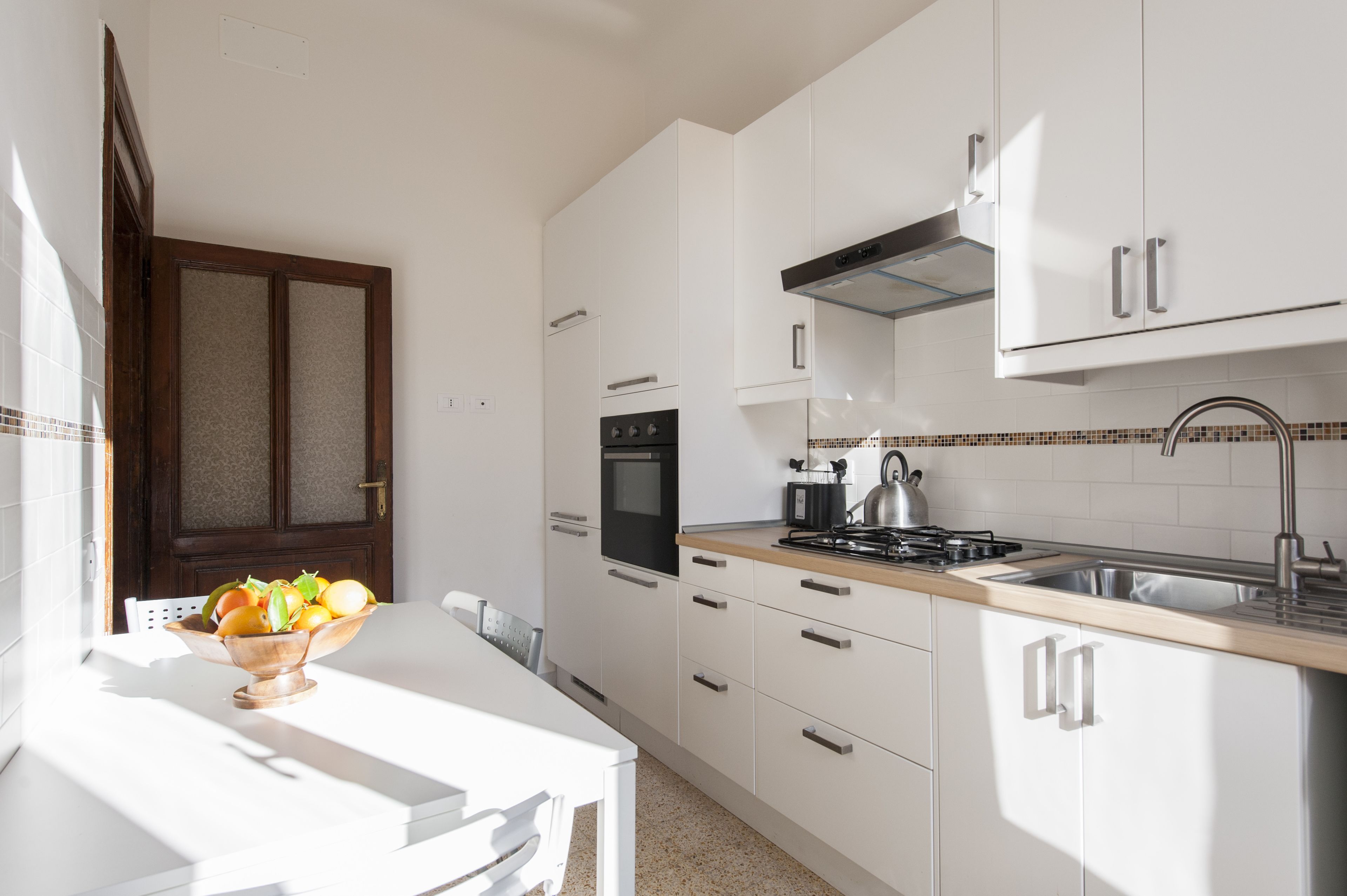 Une cuisine moderne avec des armoires blanches, un évier en acier inoxydable et un plan de travail en bois.