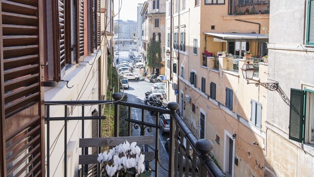 A narrow street with buildings on either side, a wooden staircase with a potted plant, and a metal railing. - Flatinrome Trastevere (Rome)