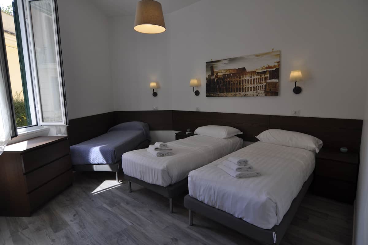 Une chambre d’hôtel avec deux lits simples, une commode en bois, une fenêtre avec des rideaux et des lampes fixées au mur.
