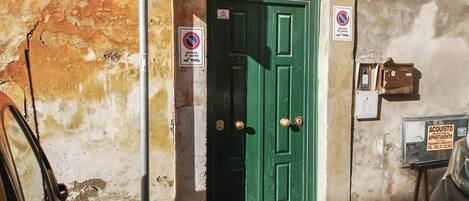 A green door with a metal grid, a no parking sign, and a mailbox with a 'For Sale' sign.