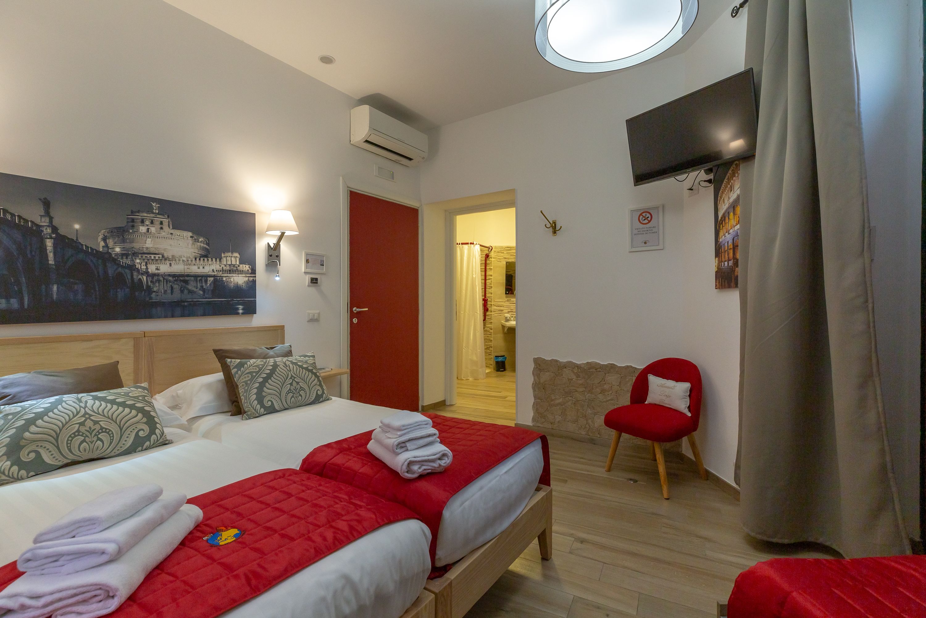 A hotel room with a large bed, a TV mounted on the wall, and a painting of a historical building.