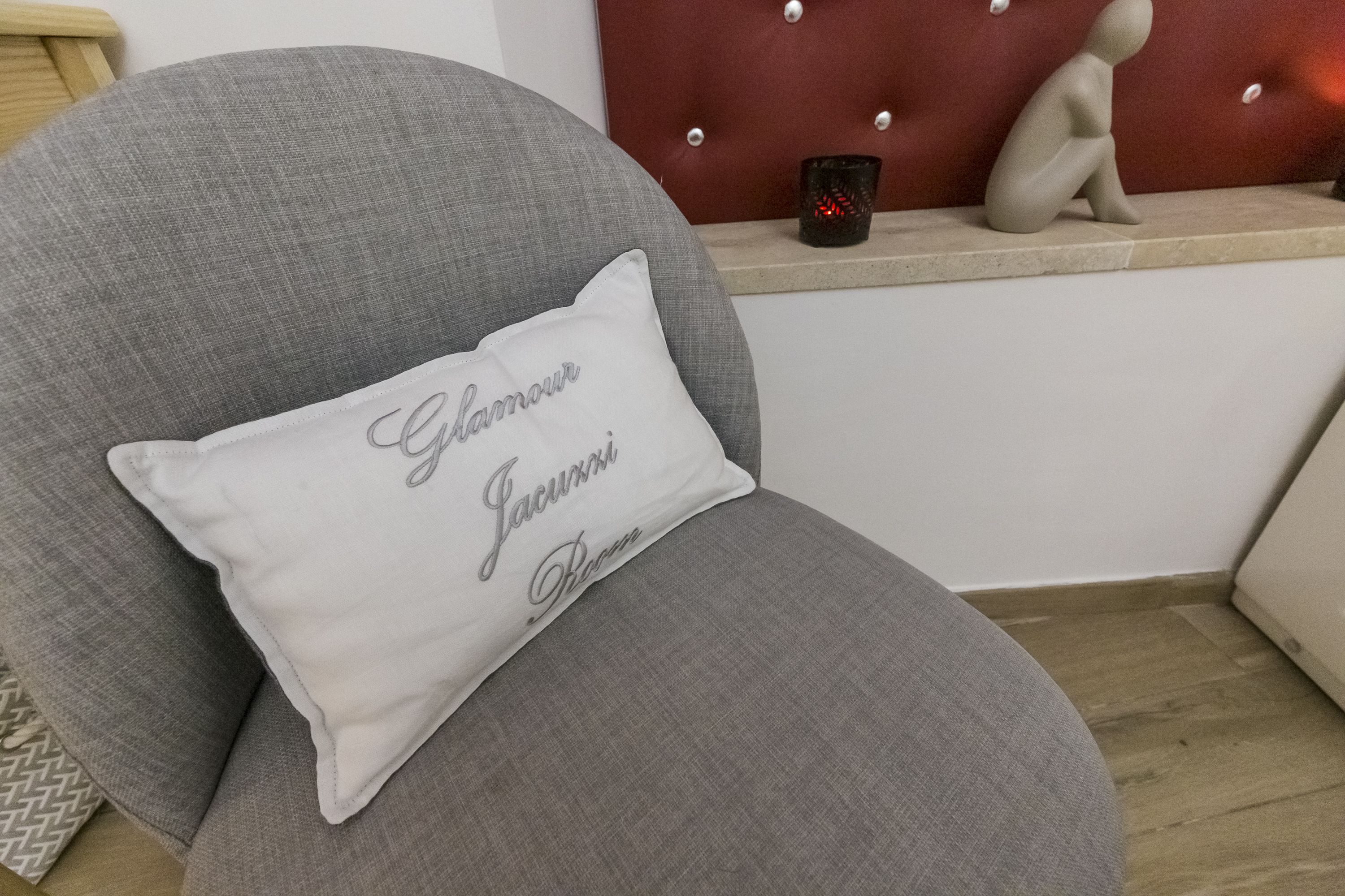 A grey upholstered chair with a white pillow that has "Lacarmes" written on it.