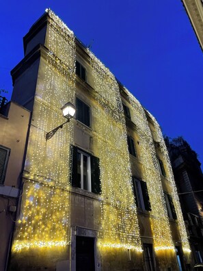 Une façade d’immeuble décorée de guirlandes lumineuses, avec de nombreuses fenêtres et une entrée bien visible.