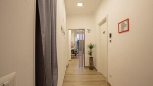 A narrow hallway with wooden flooring, a potted plant, and a door with a red-framed picture on the wall. - Flatinrome Trastevere Deluxe Rooms (Rome)