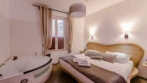 A hotel room with a bed, a wooden headboard, a bedside lamp, a window with curtains, and a bathtub. - Flatinrome Trastevere Deluxe Rooms (Rome)