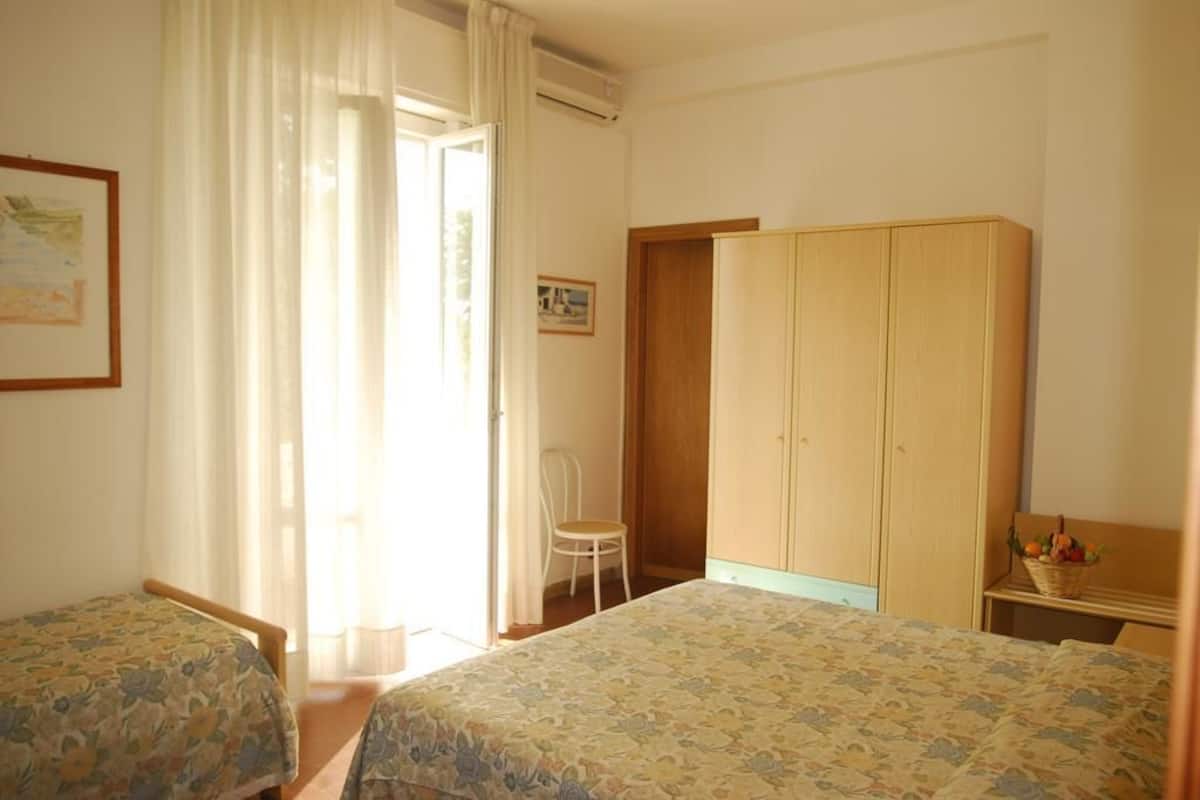 Une chambre avec deux lits, une armoire en bois, une chaise et une fenêtre avec des rideaux.
