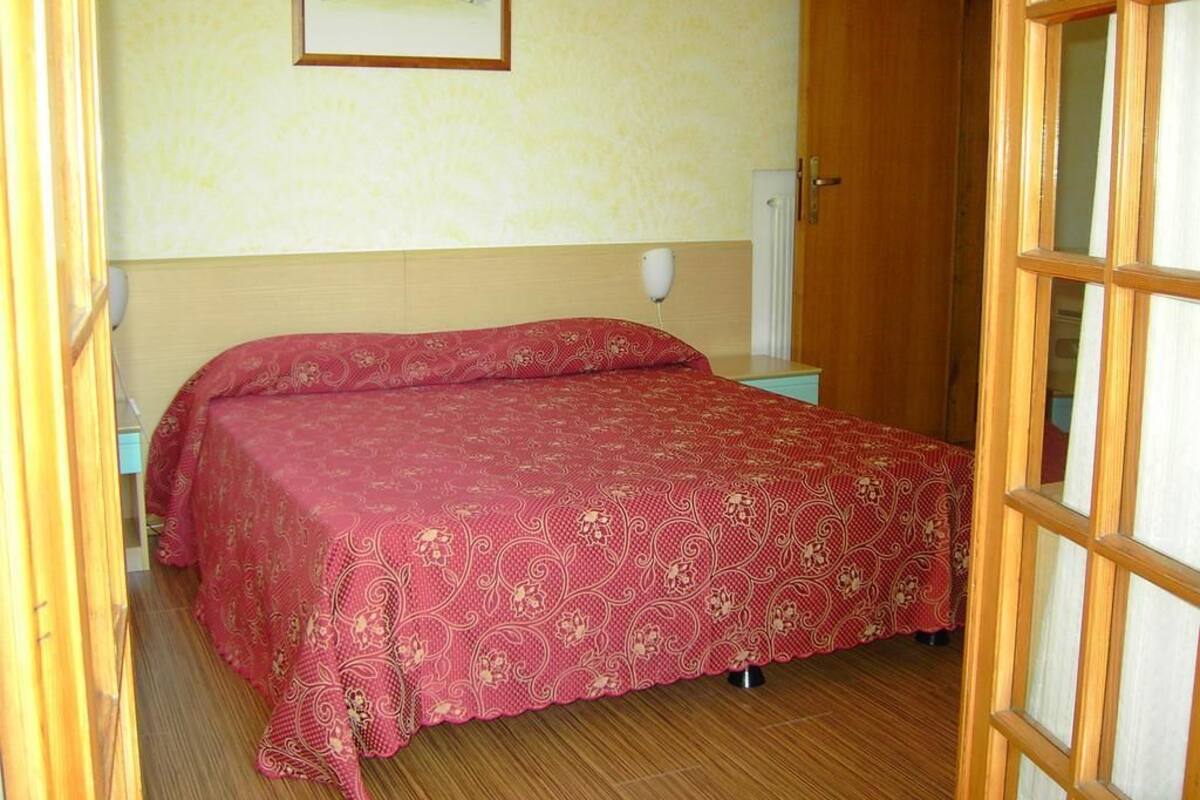 Une chambre à coucher avec un lit, une table de chevet, une lampe fixée au mur et une porte.