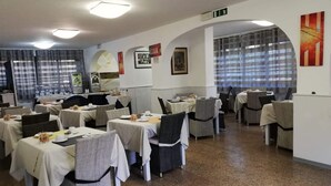 A dining area with tables set for meals, chairs, and a kitchen area in the background. - Hotel la Tavernetta dei Ronchi (Massa)