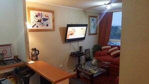 A compact living space with a kitchenette, a flat-screen TV, a red sofa, and a coffee table. - APARTAHOTEL DIARIO CONCEPCIÓN (Concepción)