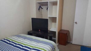 A bedroom with a bed, a TV on a stand, a wardrobe, and a small table. - APARTAHOTEL DIARIO CONCEPCIÓN (Concepción)