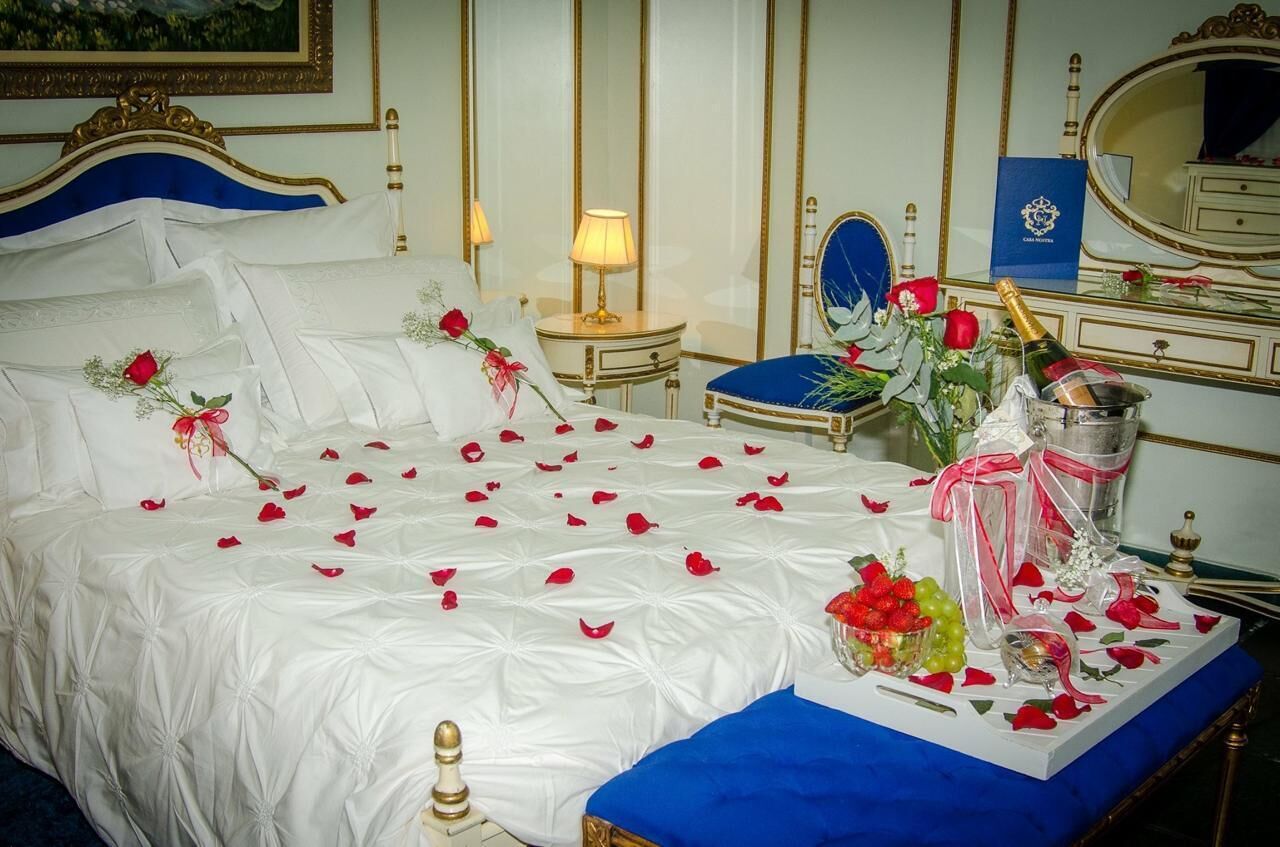 A bed with rose petals, a bottle of champagne, and a vase with flowers.