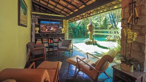 A living room with a TV, bookshelves, and comfortable seating. - Casa Nostra Boutique Hotel (Paraty)