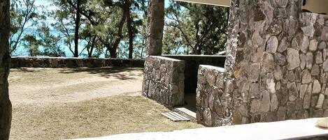 Estructura de piedra con zona de estar cubierta, pared de piedra y vistas a árboles y agua.