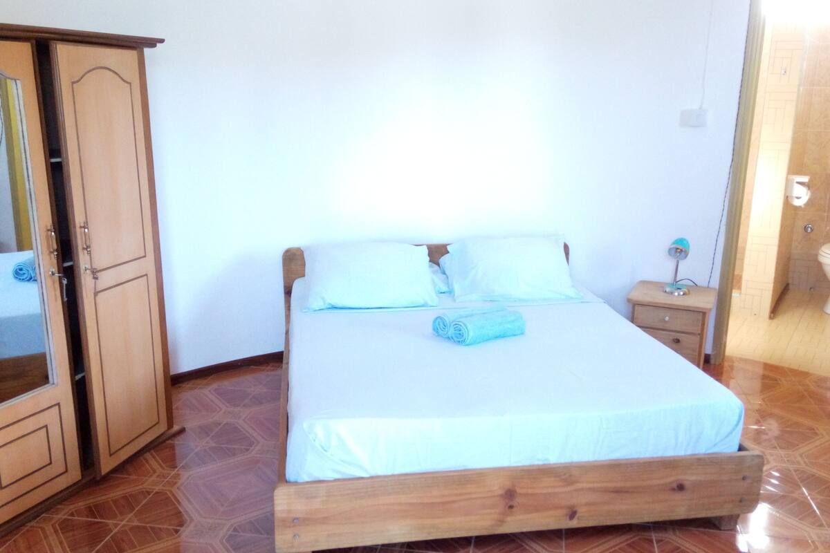 A bedroom with a wooden bed, a nightstand, a mirror, and a wardrobe.