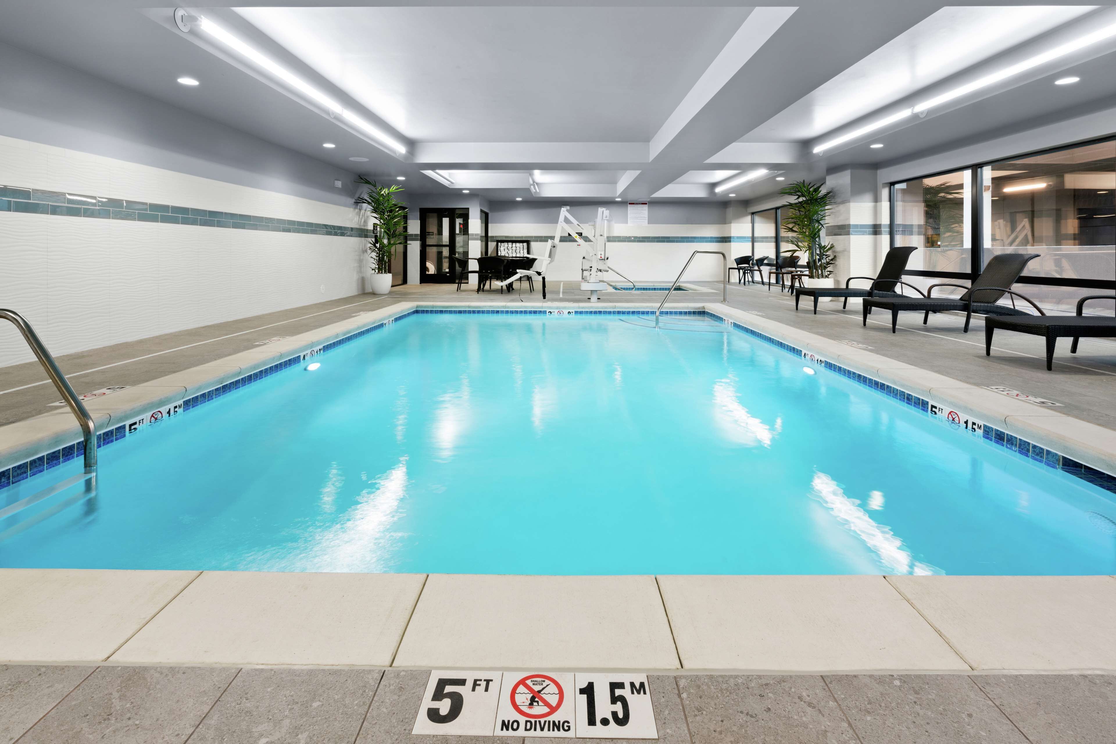 An indoor swimming pool with a no diving sign, lounge chairs, and a ceiling with recessed lighting.