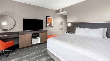 Ein Hotelzimmer mit einem großen Bett, einem Schreibtisch mit Flachbildfernseher, einem Spiegel, einem gerahmten Bild und einem Nachttisch.