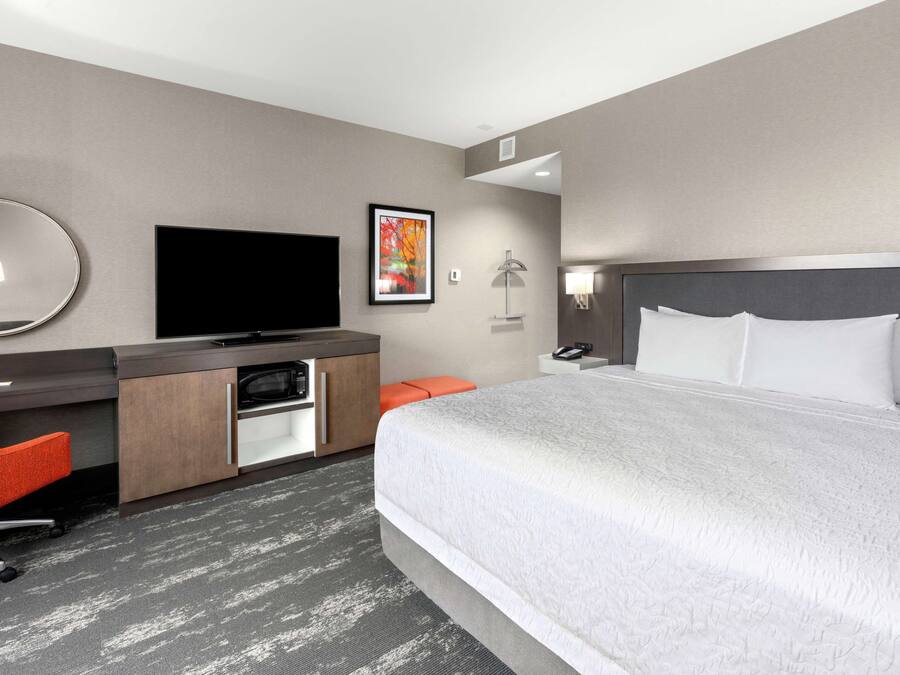 Ein Hotelzimmer mit einem großen Bett, einem Schreibtisch mit Flachbildfernseher, einem Spiegel, einem gerahmten Bild und einem Nachttisch.