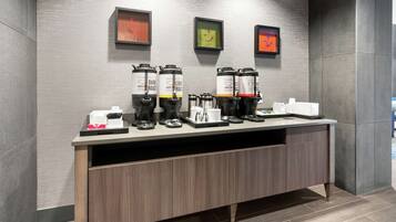 Un espace dédié au café, équipé de plusieurs machines à café et d’une cafetière, avec un comptoir blanc et un meuble en bois en dessous.