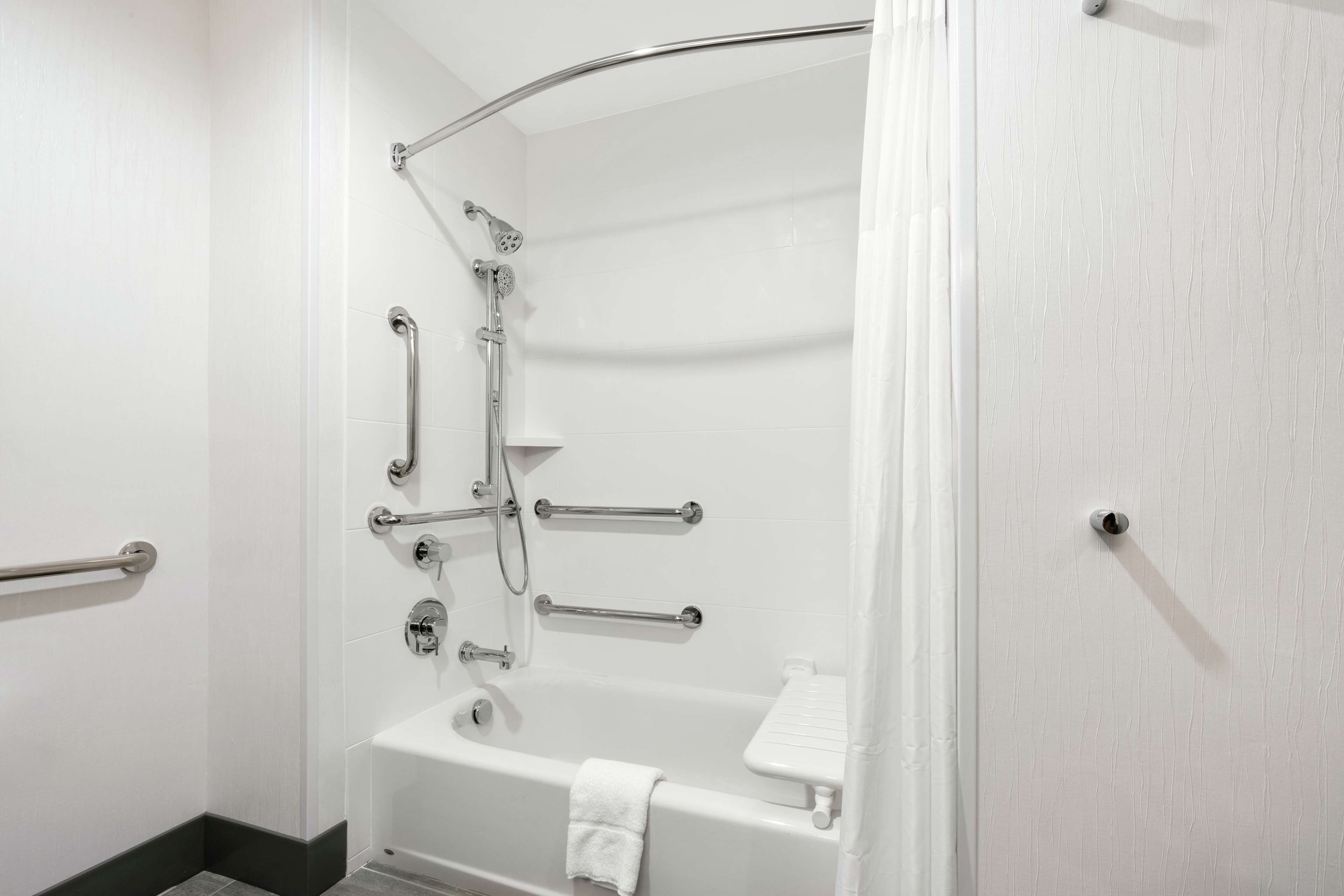 A bathroom with a bathtub, shower, and grab bars.