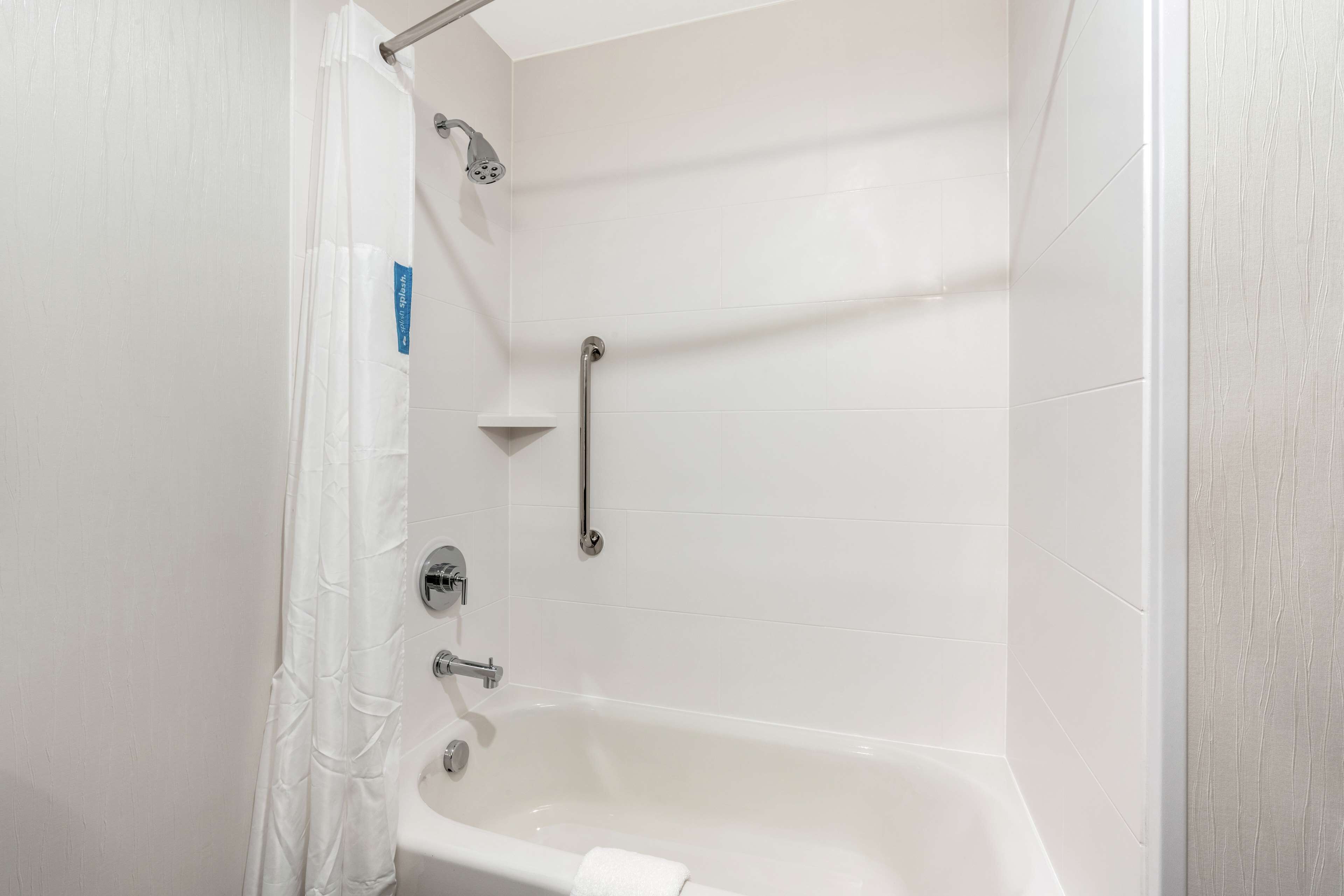 A bathroom with a bathtub, shower, and grab bar.