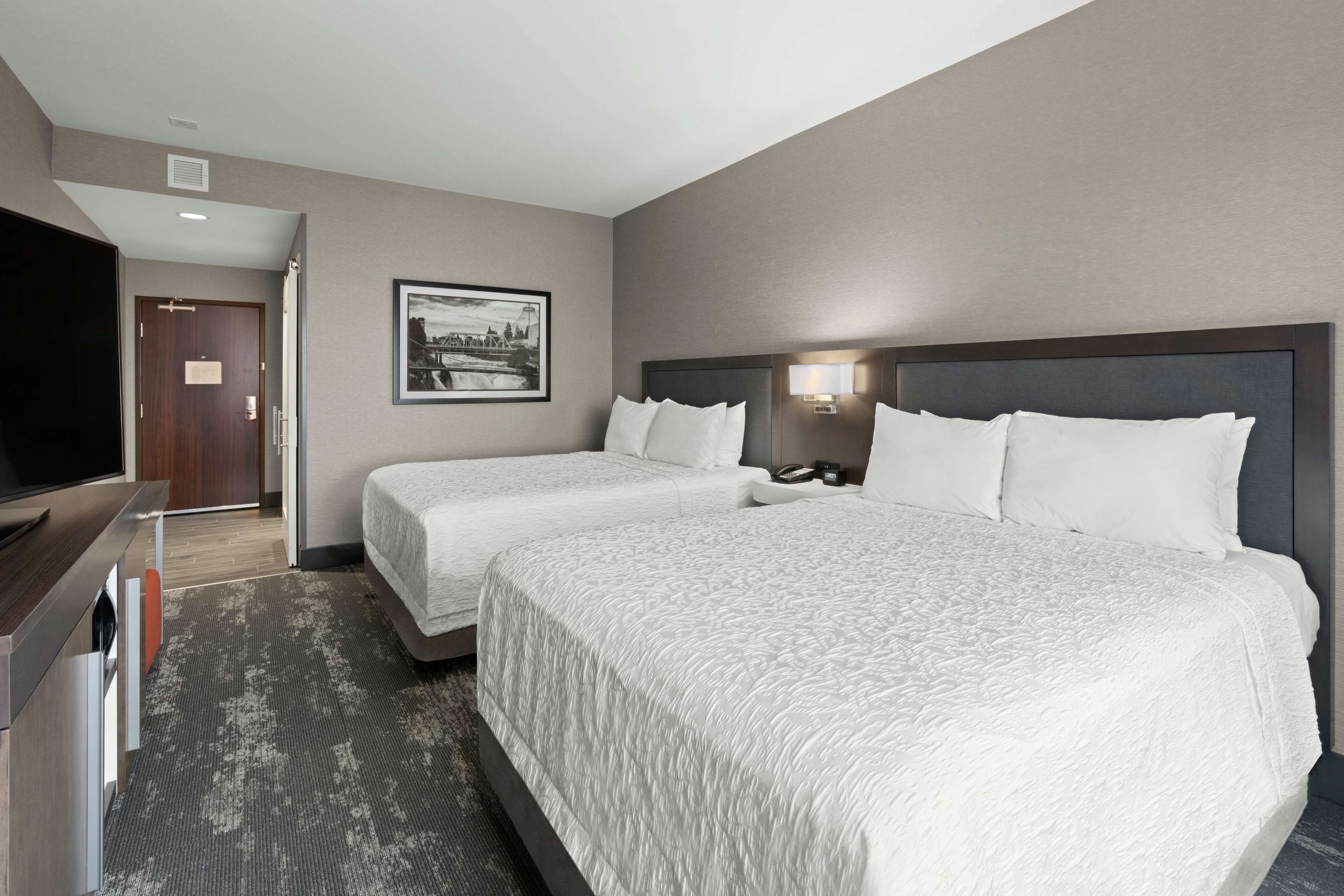 Een hotelkamer met twee bedden, een televisie, een ingelijst schilderij aan de muur en een tapijtvloer.