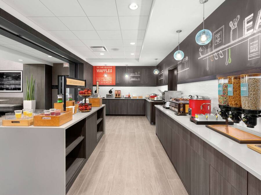 Een moderne keukenhoek met een pannenkoekenstation, koffieapparaten en diverse etenswaren op de toonbank.