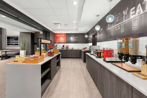 Een moderne keukenhoek met een pannenkoekenstation, koffieapparaten en diverse etenswaren op de toonbank.