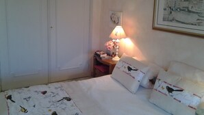 Uma cama bem arrumada com almofadas estampadas, uma luminária de cabeceira, um quadro na parede e uma porta à esquerda.