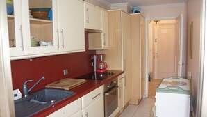 Uma cozinha compacta com bancada vermelha, cafeteira e pequena geladeira.