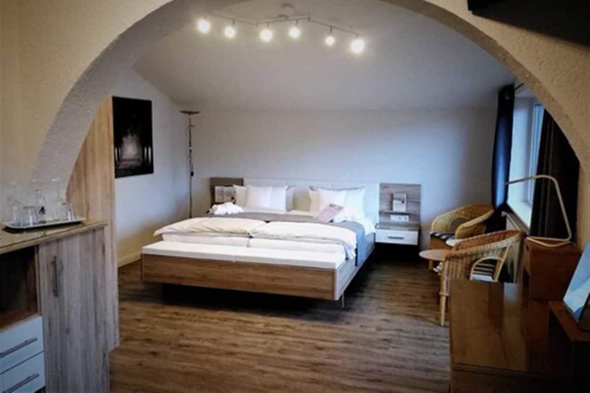 A bedroom with a large bed, a nightstand, a chair, and a desk with a lamp.