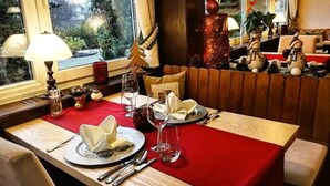 A dining area with a red tablecloth, neatly set table with plates, glasses, and cutlery. A small Christmas tree and decorative items are on the table. - Ferienhotel Schwarzwälder Hof (Feldberg)