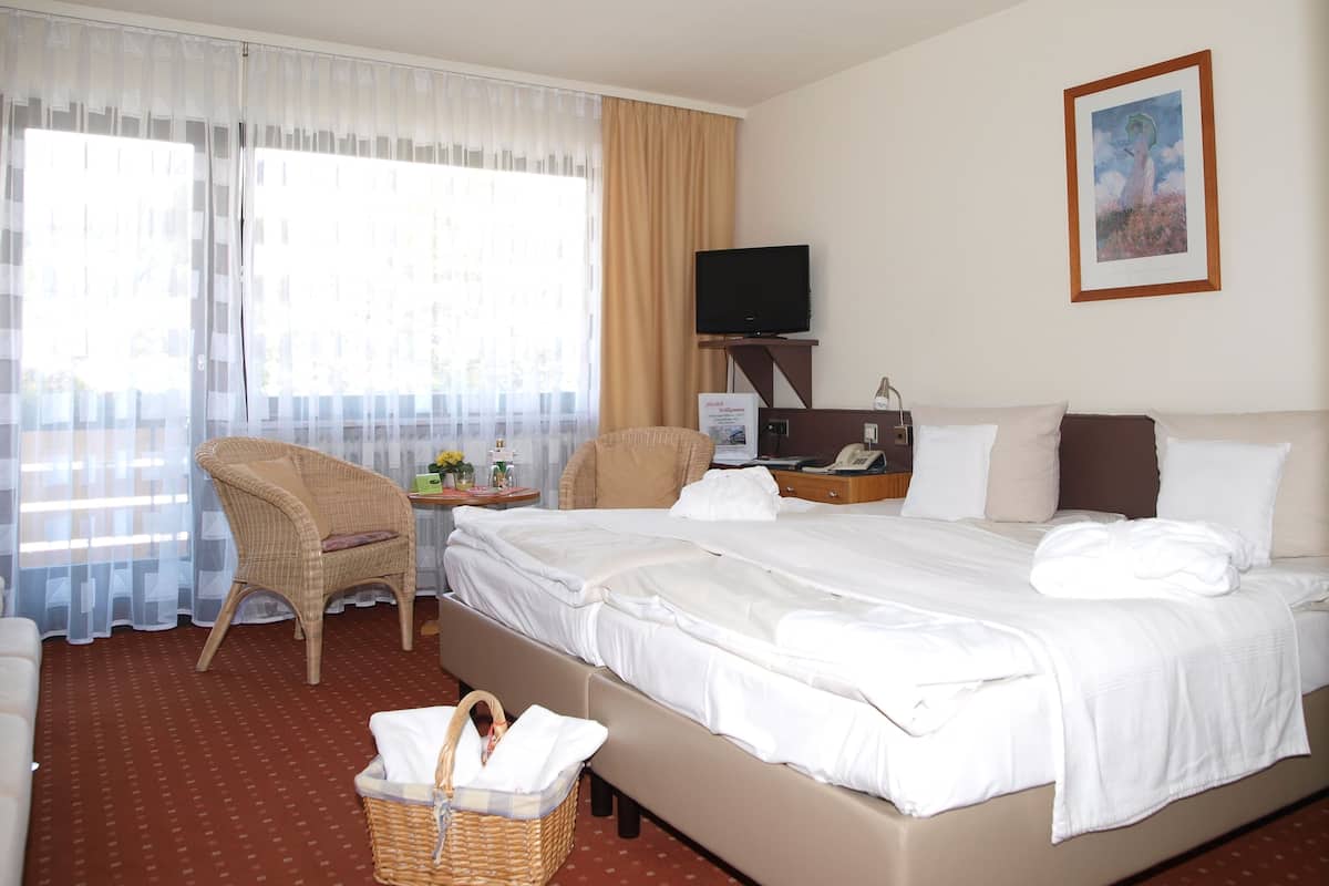 A hotel room with a bed, two chairs, a desk with a computer and phone, a television, and a painting on the wall.