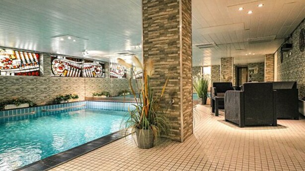An indoor swimming pool with tiled flooring, a stone wall, and a seating area with chairs. - Ferienhotel Schwarzwälder Hof (Feldberg)