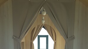 A room with a high arched ceiling, a bed with a blue mattress, and beige curtains. - Camping Le Mont Joli Bois (Criel-sur-Mer)