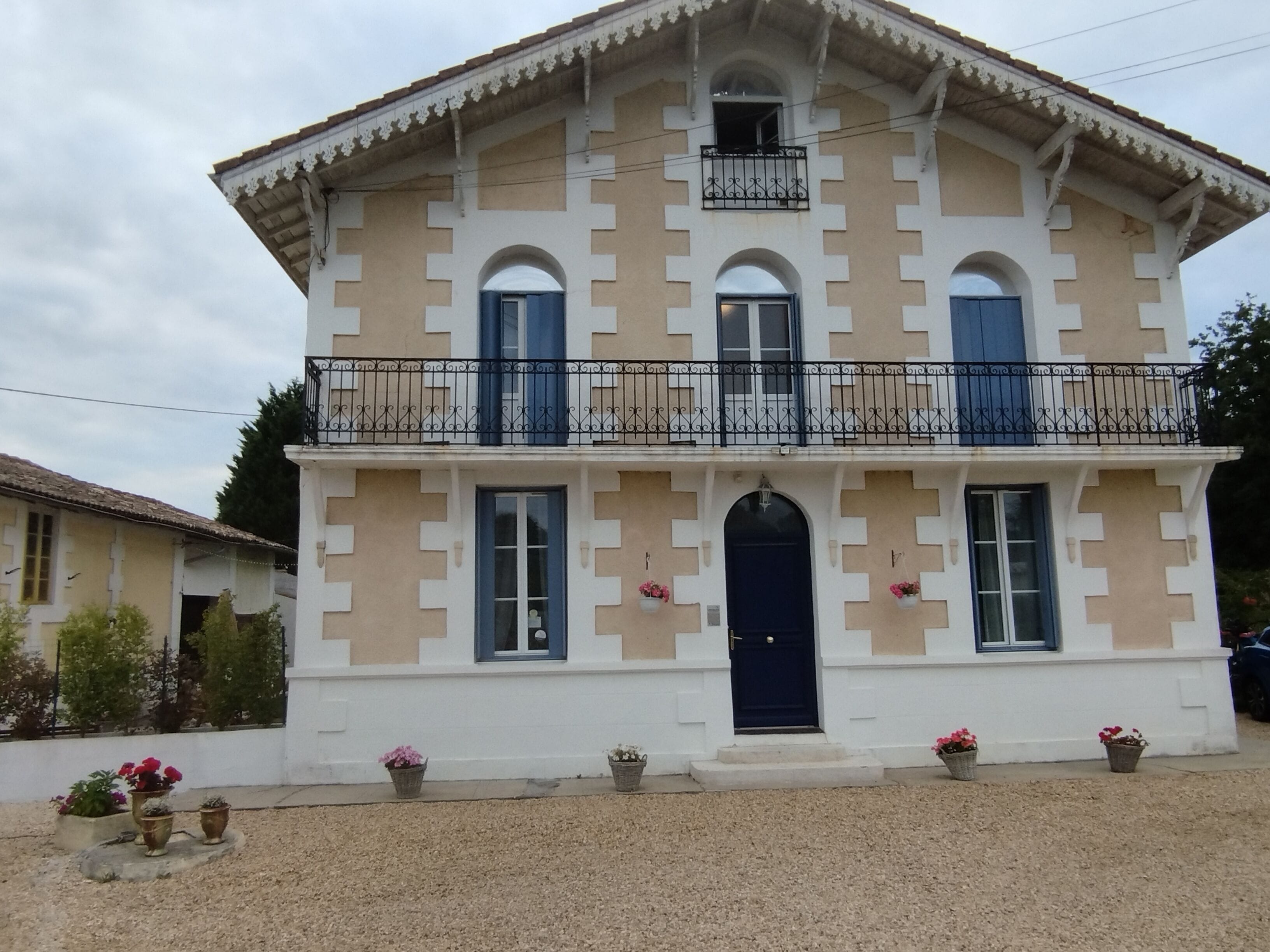 Un bâtiment à deux étages doté d’une façade symétrique, d’une entrée centrale avec une porte sombre et d’un balcon orné de balustrades décoratives.