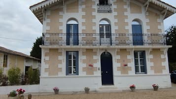 Un bâtiment à deux étages doté d’une façade symétrique, d’une entrée centrale avec une porte sombre et d’un balcon orné de balustrades décoratives.