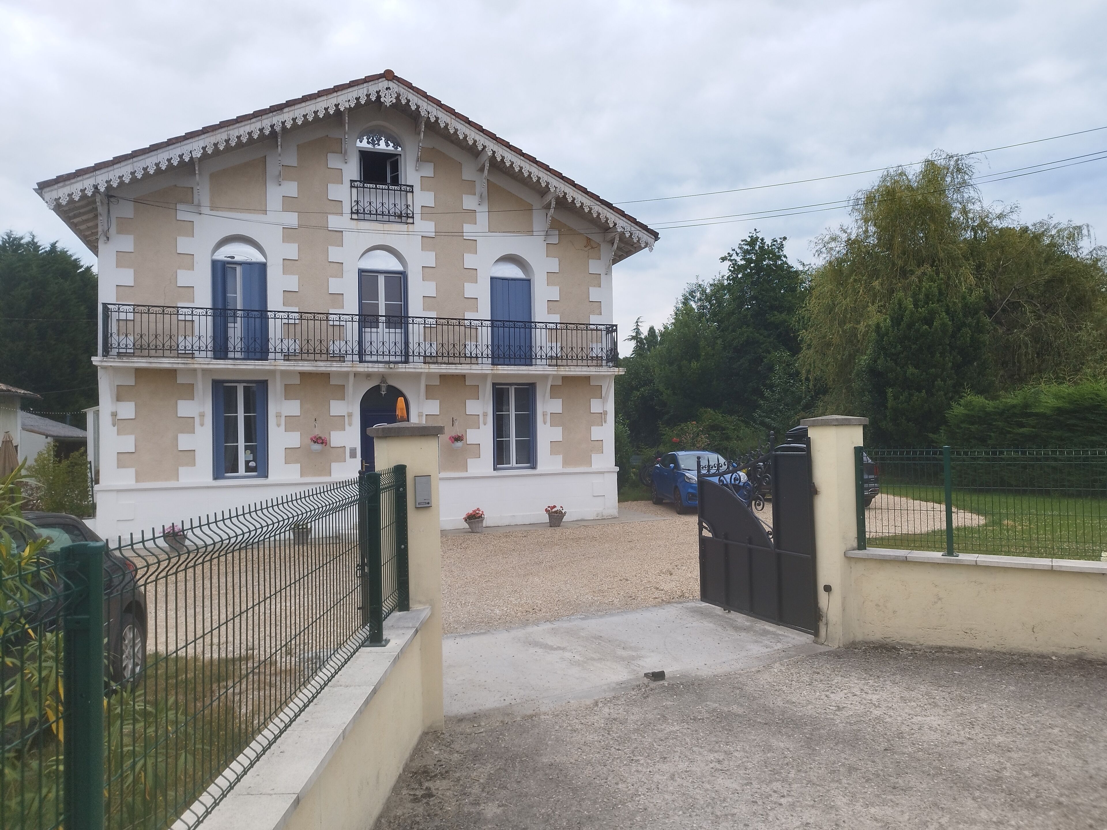 A two-story building with a balcony, a gated entrance, and a gravel driveway.