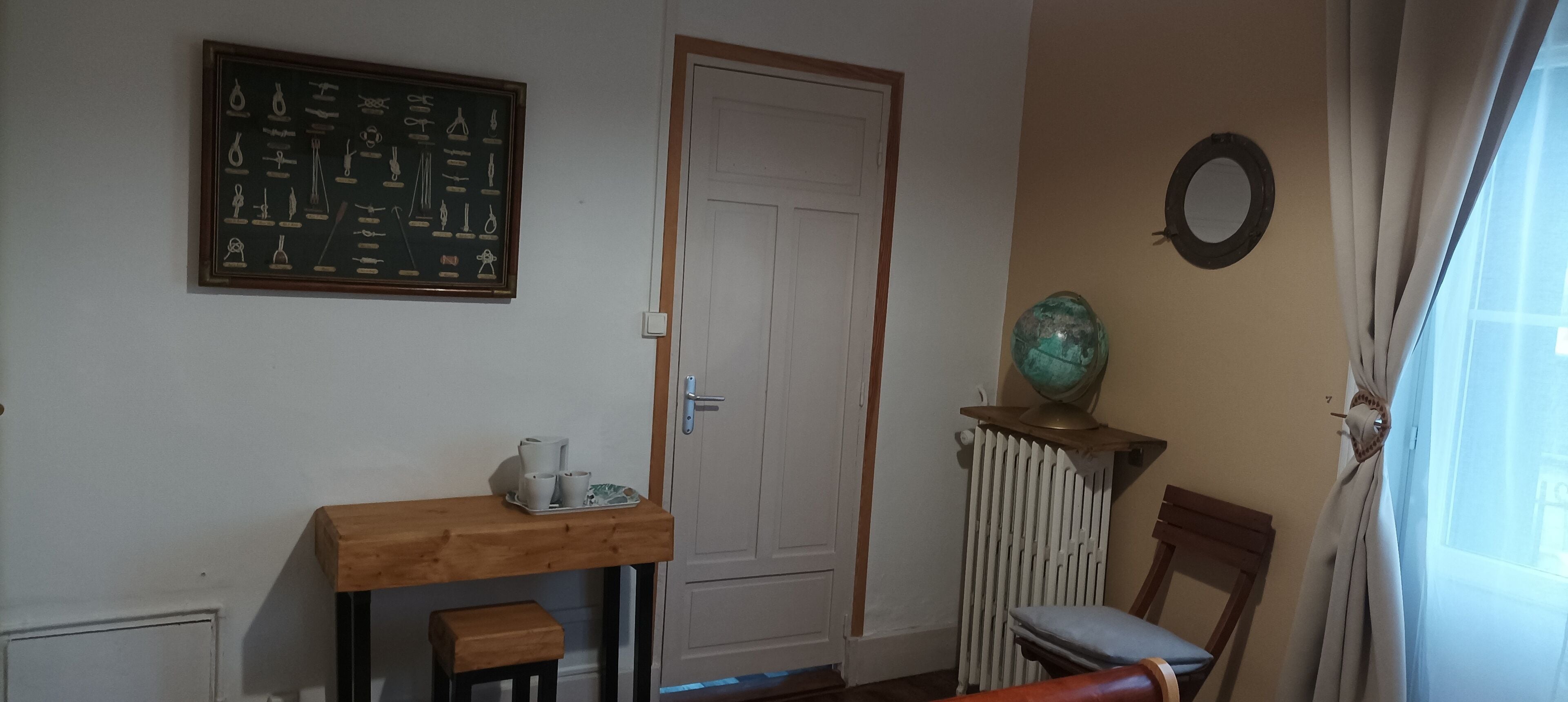 Une pièce comprenant une table en bois, une chaise, un radiateur, une porte et un globe terrestre posé sur un socle.