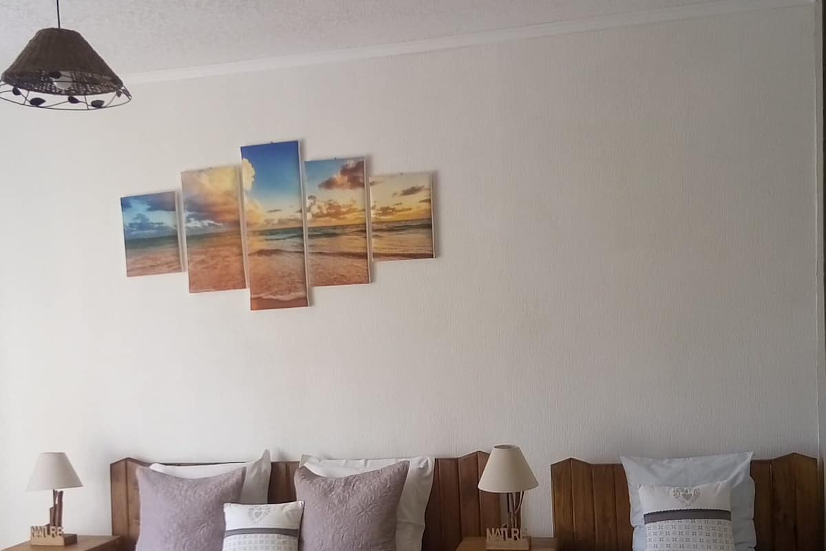 A bedroom with two beds, a ceiling fan, and a wall with three paintings.